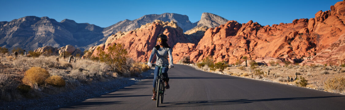 fit african american woman riding bicycle on road in red rock canyon park panorama