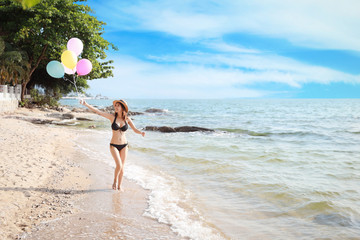 happiness on holiday image of young asian beautiful and sexy girl in black bikini who holding balloons and running on sandy beach with happy and smile face on sunny day and summer time