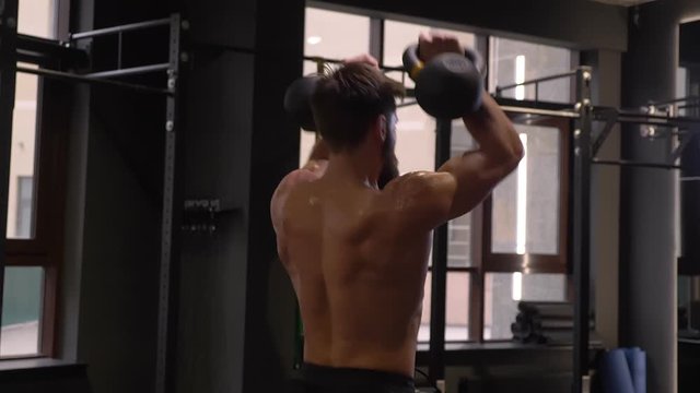 Closeup back view shoot of adult muscular athletic man making squats with the kettlebells indoors in the gym