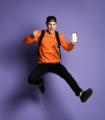 Handsome young student man in casual wear with backpack and headphones is listening to music using a smartphone and smiling while jumping
