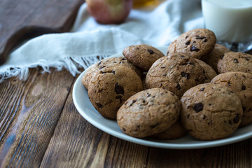 Pile of Delicious Chocolate Chip Cookies on a plate with glass of milk on wooden table