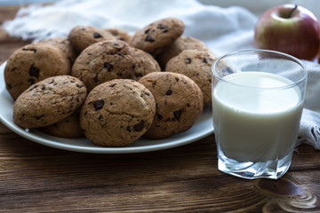 Pile of Delicious Chocolate Chip Cookies on a plate with glass of milk on wooden table