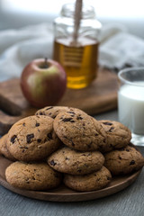 Pile of Delicious Chocolate Chip Cookies on a plate with glass of milk on wooden table