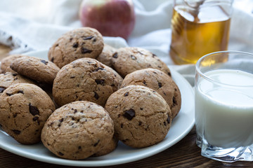 Pile of Delicious Chocolate Chip Cookies on a plate with glass of milk on wooden table
