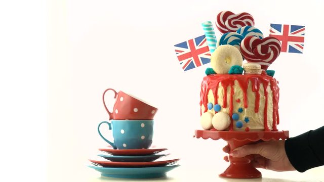 UK on-trend candyland fantasy drip cake with red, white and blue decorations, lollipops and flags on white background.