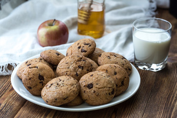Pile of Delicious Chocolate Chip Cookies on a plate with glass of milk on wooden table