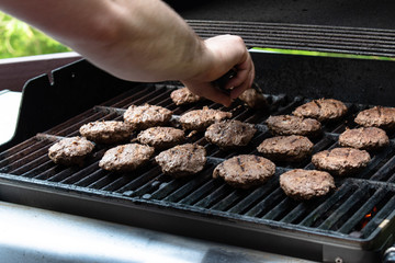 Male hand grilling burgers on a grill