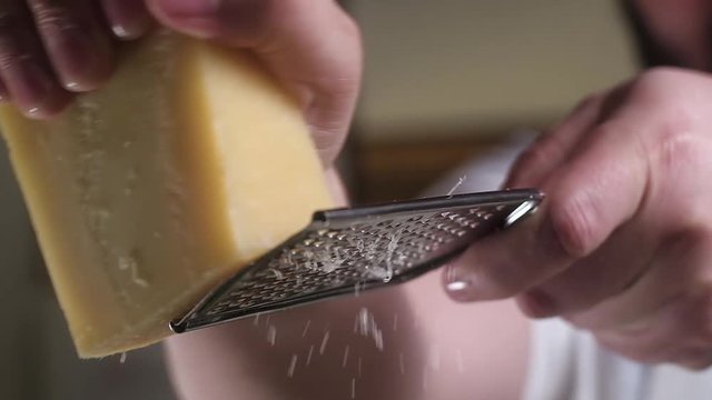 large piece of Parmesan cheese is rubbed on a metal grater. Close up. Slow motion.