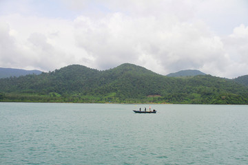 A small boat out fishing in the middle of the sea with the natural of the mountains and forests in the background.