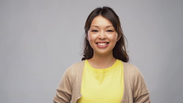 portrait, emotions and people concept - smiling young asian woman in cardigan over grey background