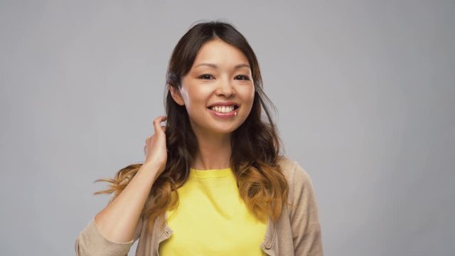 portrait, emotions and people concept - smiling young asian woman touching her dyed hair over grey background
