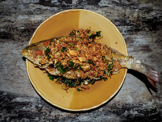 Fried fish with Thai herb are kaffir lime leaves and garlic serve in brown plate
