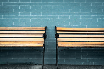 Empty two wooden bench on green brick wall background. Waiting for someone to full fill empty wooden chair. Brown wooden bench outside the building. Waiting concept. Empty wall with space for quote.