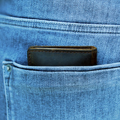 Brown men's wallet of quality genuine leather lies in the back pocket of men's blue jeans, square