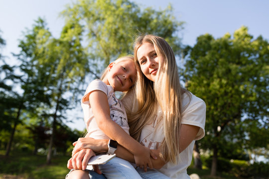 Beautiful Young Mother And Daughter With Blonde Hair Embracing Outdoor. Stylish Girls Making Walking In The Park. Family Concept