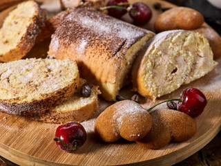 Rolled biscuit and sand chocolate cookies on board. Cinnamon stick and cherry on kitchen wood table in rustic style. Breakfast for loved one.