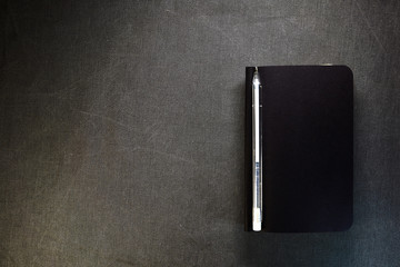 Top view of closed black cover notebook with pencil on gray background