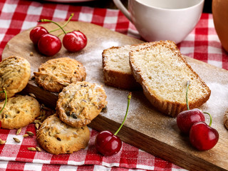 Oatmeal cookies and cherry on kitchen cutting board gingham checkered cotton fabric on table in village style for picnic. Best selection of sweets. Beautiful, expensive, culinary masterpieces.