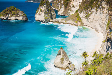 Tropical beach with coconut palms and rock in Nusa Penida, Bali, Indonesia.