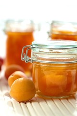 Apricot jam. Orange jam in glass jars , fresh ripe apricots on a wooden white table on a light background. High key.Homemade jam.Summer  Canned fruit jam. Healthy vegetarian sweets