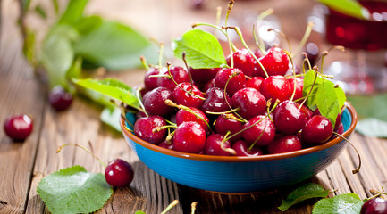 Fresh sweet cherries bowl with leaves in water drops on wooden background, top view