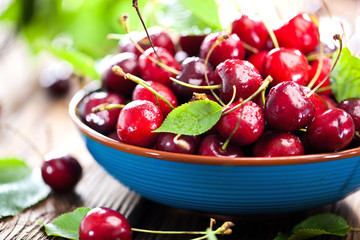 Fresh sweet cherries bowl with leaves in water drops on wooden background, top view
