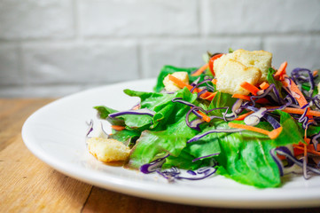 Salad of fresh vegetables in a white plate, placed on an old wooden table, close up.