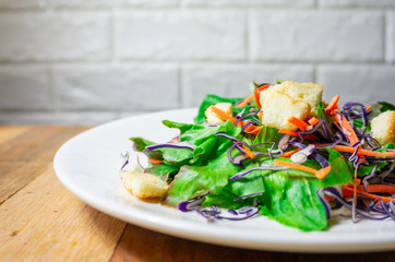 Salad of fresh vegetables in a white plate, placed on an old wooden table, close up.