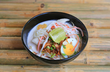 Noodle in coconut milk soup in bowl on bamboo wood table. Fusion Thai food.