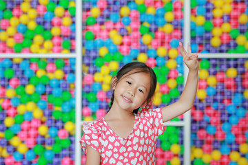 Beautiful Asian little girl doing thai style dance expressions against colorful toy ball playground. Expresses pleasant emotions.