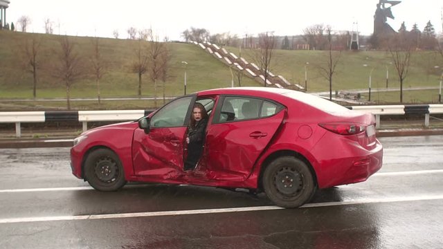 The girl slowly gets out of the car which had just crashed, she's in shock and she's scared. The girl flew into a pole at the speed of the car in the rain or snow. Slow motion.
