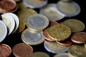 Pile of Euro coins scattered on a dark surface close up