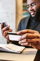 Close up shot of African man's hands holding mobile and credit card