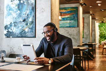 Fototapeta premium Go and get your things. Dreams mean work. Young businessman with tablet pc and headphones sitting in cafe and networking