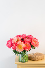 Coral peonies in a glass vase and wicker bag on wooden table.. Beautiful peony flower for catalog or online store. Floral shop concept . Beautiful fresh cut bouquet. Flowers delivery. Copy space