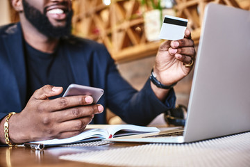 The time making money should be greater than the time that you are spending money. Close up shot of African man's hands holding mobile and credit card.