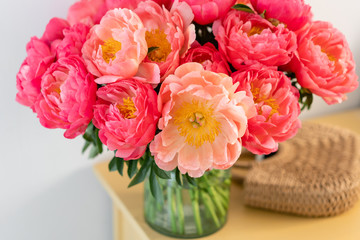 Coral peonies in a glass vase and wicker bag on wooden table.. Beautiful peony flower for catalog or online store. Floral shop concept . Beautiful fresh cut bouquet. Flowers delivery. Copy space