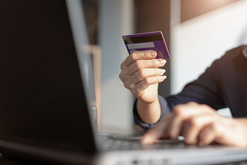 Woman's hands holding credit card and typing on the keyboard of laptop for shopping online. Pays for purchase.