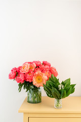 Coral peonies and spring lilies of the valley in a glass vase on wooden table.. Beautiful peony flower for catalog or online store. Floral shop concept . Beautiful fresh cut bouquet. Flowers delivery.