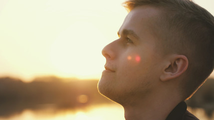 Close up portrait of pensive handsome young man looking up enjoying nature in sun rays at sunset