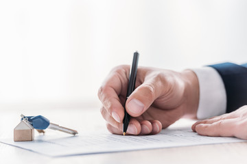 cropped view of businessman writing in agreement and car keys on tabletop