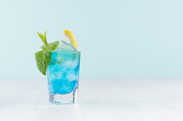 Summer fresh blue curacao cocktail with lemon slice, ice cubes, mint in wet shot glass on white...