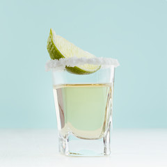Refreshing tequila drink with slice lime, salt in shot glass on soft light white wood board and...