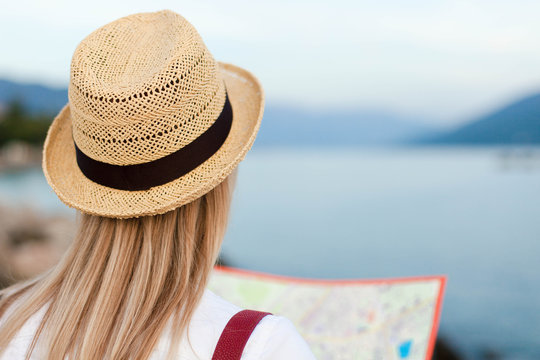 Traveler is looking at map at sea beach. Woman tourist is traveling. Girl in straw hat is enjoying summer vacation. Concept of student travel, solo female tourism, adventure, trip, journey.