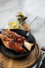 Gegrillte Schweinefleisch Haxe in gusseiserne Pfanne auf Holzbrett mit Cornichons, süßen und mittelscharfen Senf auf Marmor Hintergrund