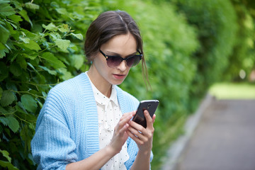 Pretty woman reads sms on mobile phone in the city park