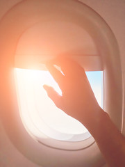 Passenger's hand closing the window shade on a modern airplane.