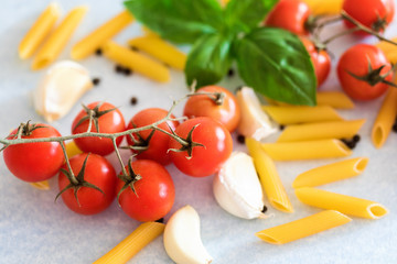 Penne pasta with cherry tomatoes, garlic cloves and basil leaves at table, close-up