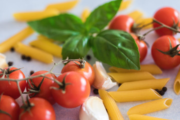 Penne pasta with cherry tomatoes, garlic cloves and basil leaves at table, close-up