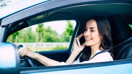 Smiling young woman talking on the phone while driving a car